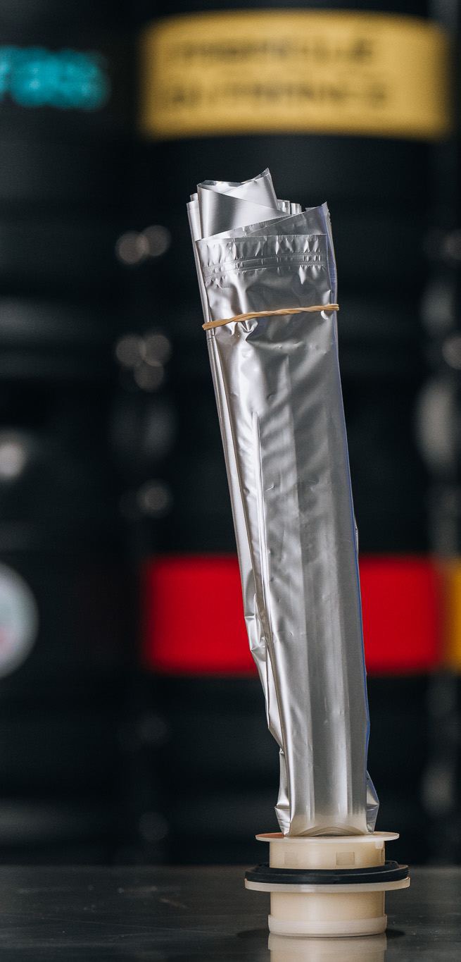 Poche aluminium ECOFASS debout sur sa tête de tirage, devant un rack de fûts